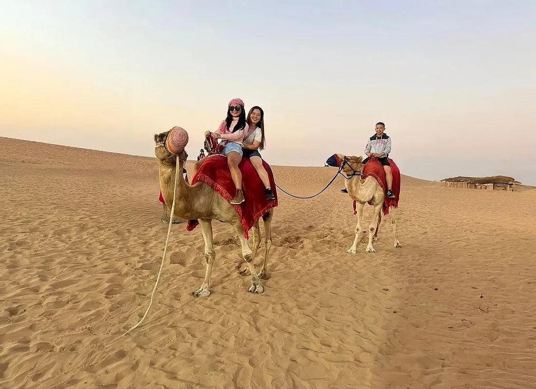 Two guests riding a camel led by a handler across a dune at golden hour on a Dubai desert safari