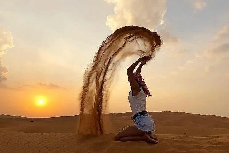 A guest kneeling on a dune and throwing a stream of sand into the air at the designated desert safari photo stop