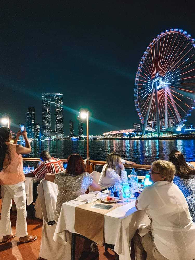 Guests dining on deck with a lit-up Ain Dubai wheel in the background