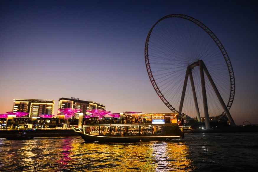 Traditional wooden dhow cruising Dubai Marina at night with illuminated skyline
