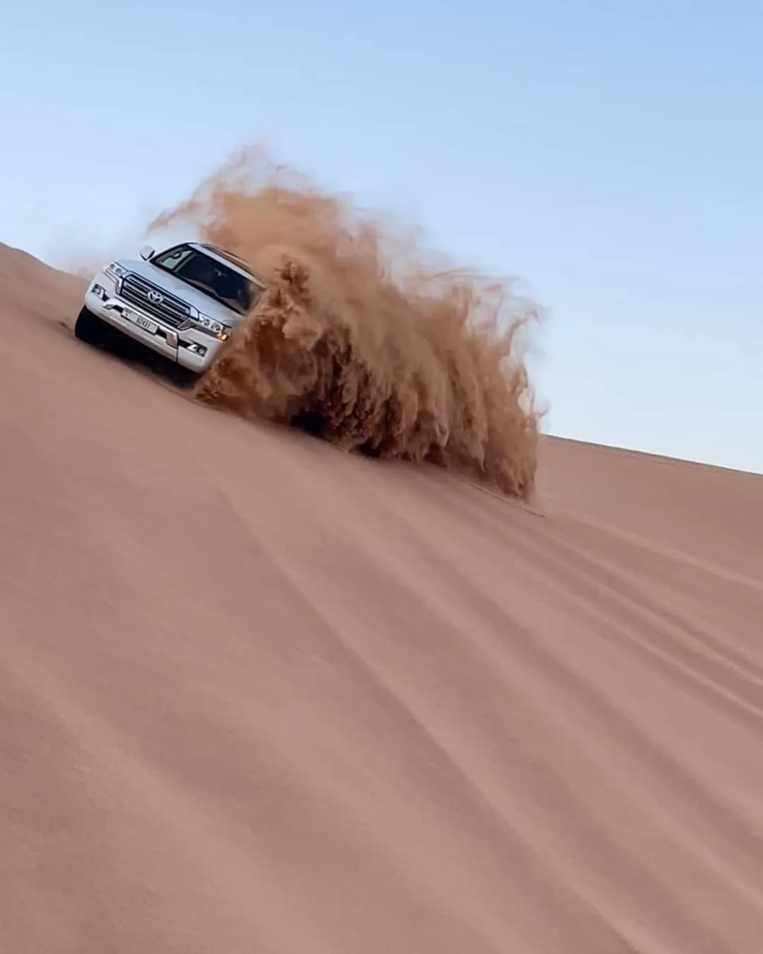 A white 4x4 kicking up sand while dune bashing under a clear blue morning sky in Dubai