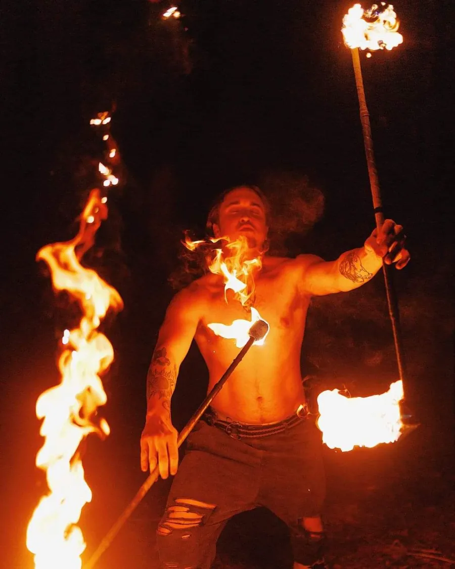A fire performer holding two flaming torches during a live show at a Dubai desert safari camp at night