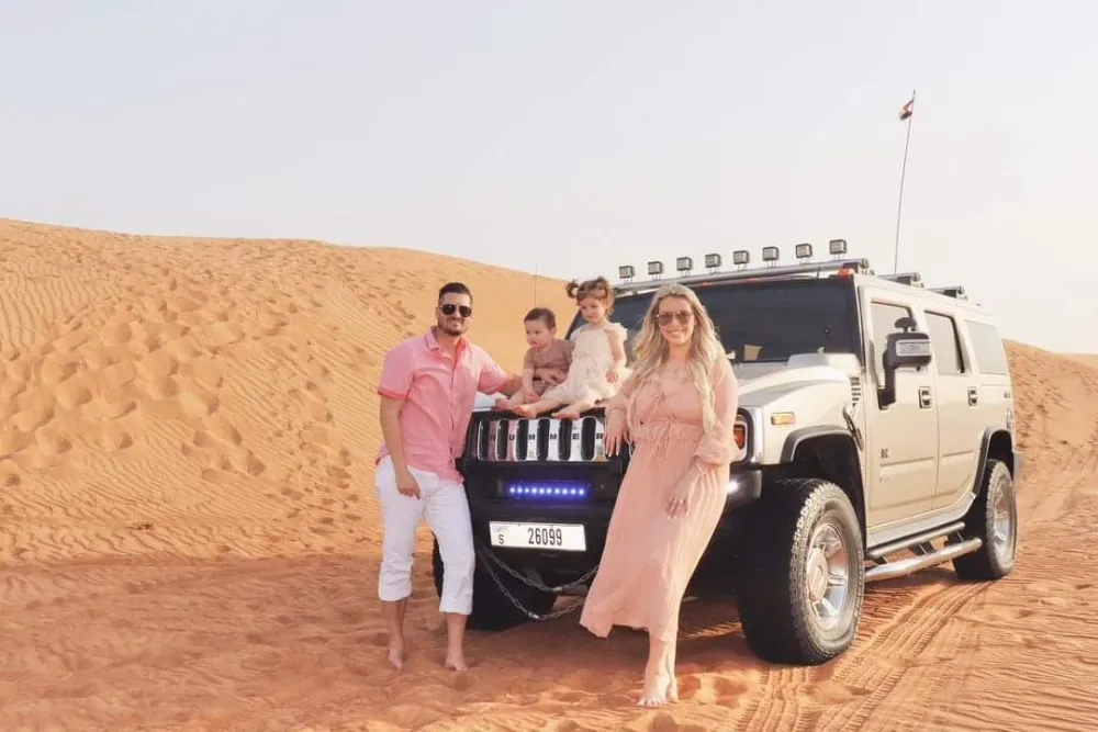 A family posing in front of a white Hummer H2 desert safari vehicle in the dunes