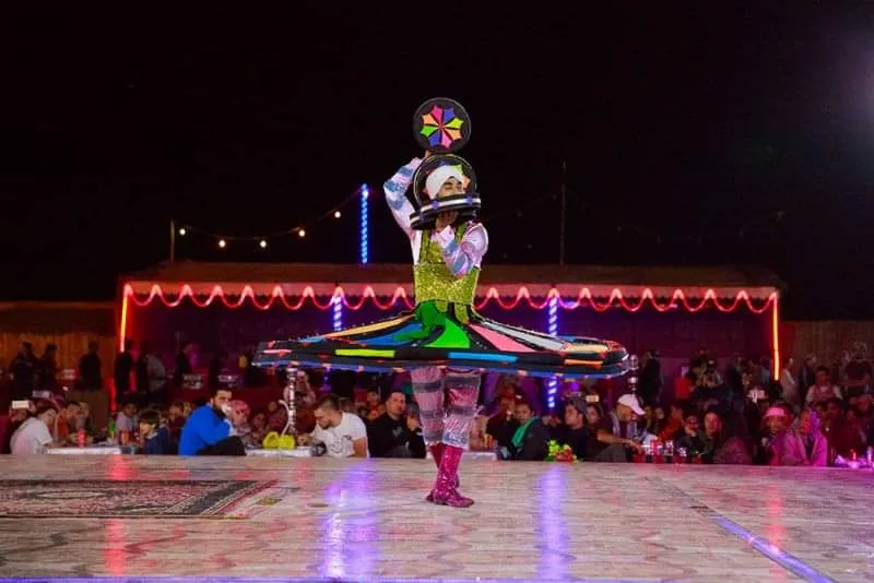 A tanoura dancer in an illuminated LED skirt performing at night in a decorated Dubai desert safari camp